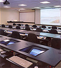 Computer classroom with monitor screens inserted at an angle in the desktops with smartboard at the front of the classroom