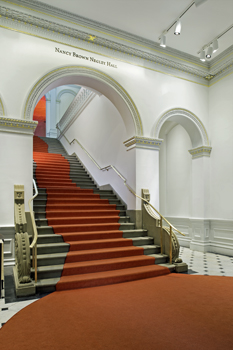 Grand stair in the Renwick Gallery after renovation shows restored rails, risers, and a curving red carpet runner.