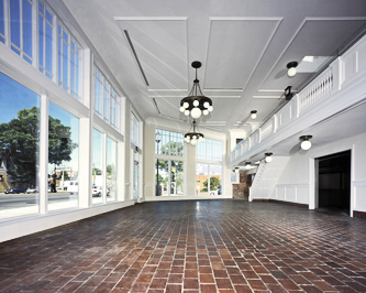 Interior of a former auto showroom showing the mezzanine with brick flooring, white painted woodwork, detailed celing with white globe chandeliers