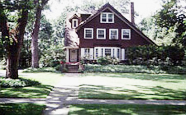 multi-story red brick home with lots of windows and a sloping roof, landscaping and trees, a large grassy yard and a path leading up to the front door on the left