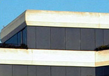 top floors of the exterior of an angular building with white trim yellowing from lack of upkeep and tinted windows