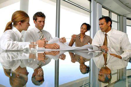 Four people sitting around a glass conference table looking over plans