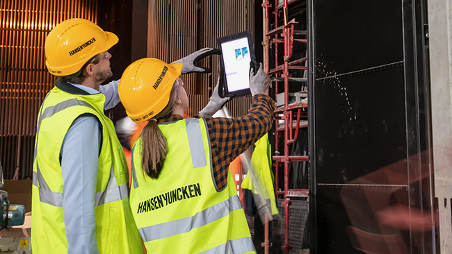 stock photo of two workers in hard hats and high viz vests in a wareshouse looking at a tablet