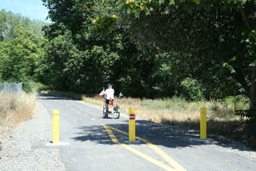 man on a bicycle moving away from three bollards along the American River Trail in Redding, CA
