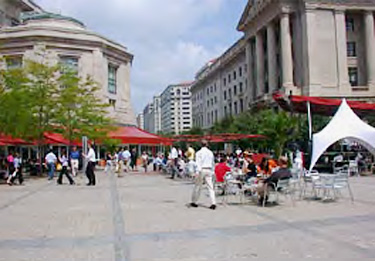 plaza space between office buildings featuring vendors under awnings, wide spaces for pedestrians, and tables and chairs for seating