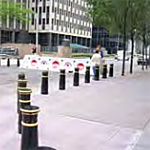 Street setting with a row of decorative black bollards with white trim mounted on concrete sidewalk