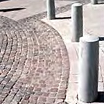 Plain bollards mounted in concrete forming a curve adjacent to a highly decorative curved paver design