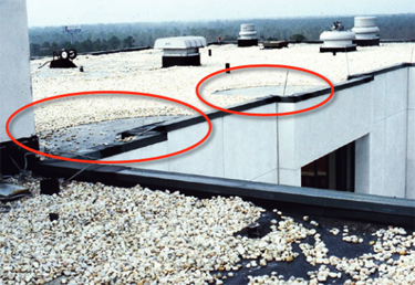 Photo of a single-ply membrane roof where the aggregate ballast was blown away in the vicinity of the corners of the wall projections at the window bays