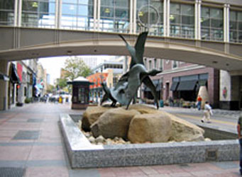 A low walled box along a curb to restrict vehicles featuring large stones and a bronze sculpture