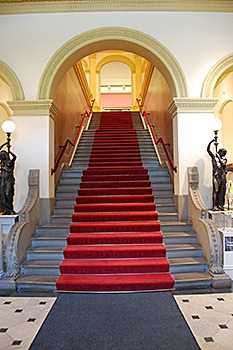 Grand stair in the Renwick Gallery prior to renovation shows gray risers and a dark straight red carpet runner