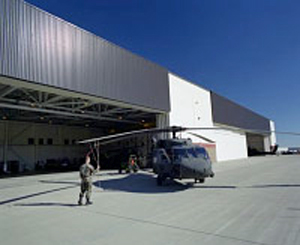 Photo of a man in front of a helicopter at Fort Carson U.S. Army Base, south of Colorado Springs, Colorado. A SolarWall solar ventilation air preheating system can be seen attached to the AVUM helicopter maintenance hangar.