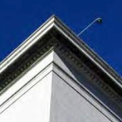looking up toward a rooftop where a surveillance camera can be seen overhanging the edge