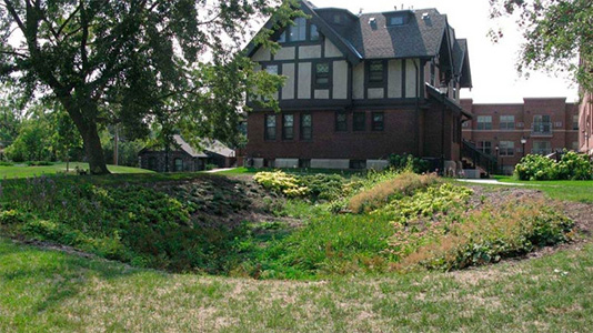 A bio-swale, or depression in the earth, created to redirect rainwater away from the storm sewer system with a large house in the background