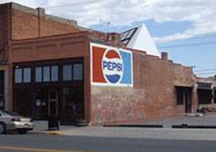 Brick building with Pepsi log painted on the side and solar panel system visible on the back of the roof